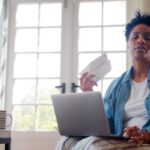 Woman fanning herself at home with laptop researching HRT help for anxiety and perimenopause mood changes