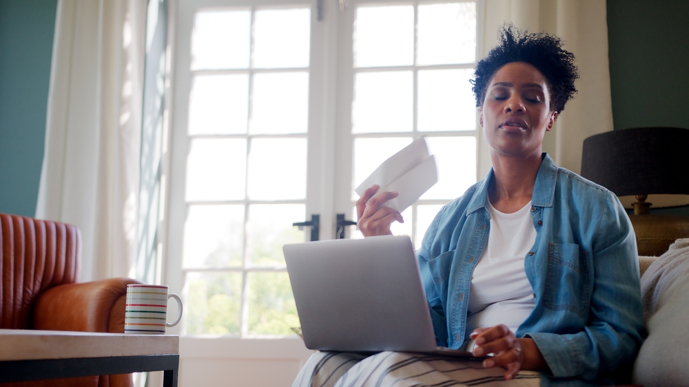 Woman fanning herself at home with laptop researching HRT help for anxiety and perimenopause mood changes