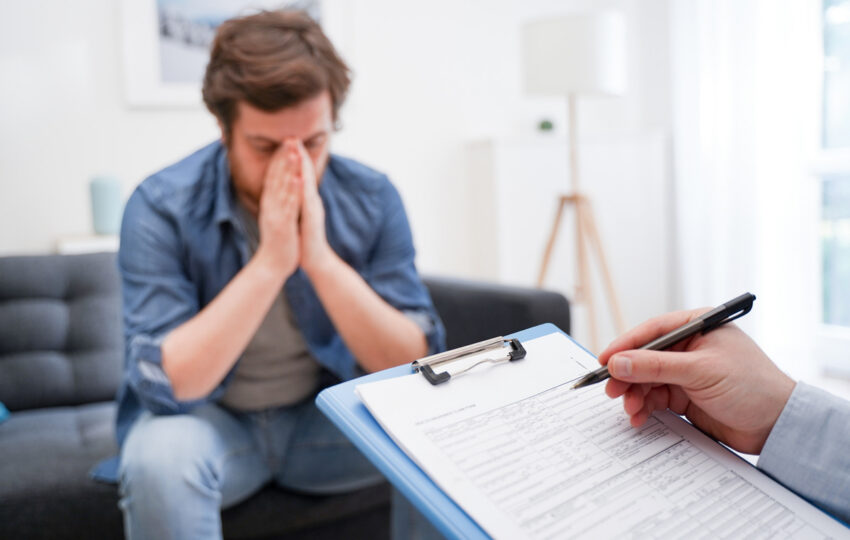 Man with head in hands showing signs of low testosterone and mental health distress while a provider takes notes during a clinical consultation