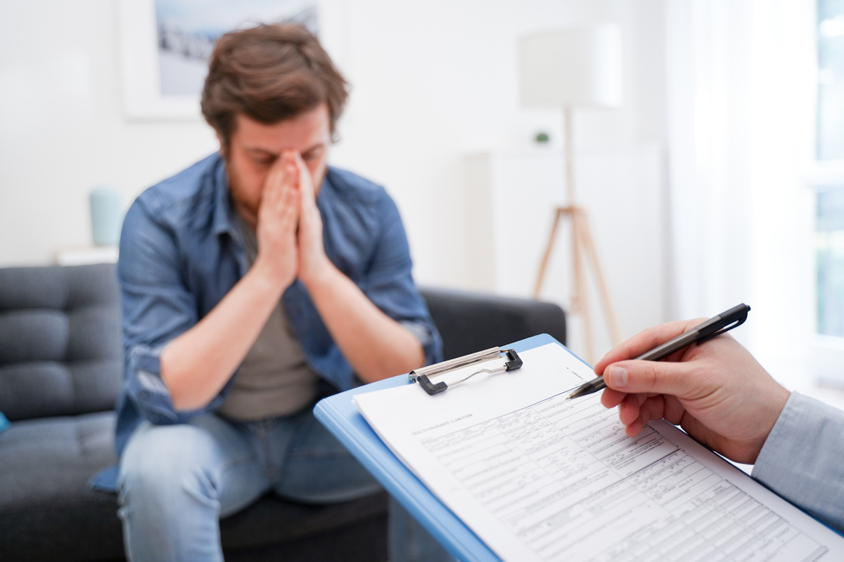 Man with head in hands showing signs of low testosterone and mental health distress while a provider takes notes during a clinical consultation